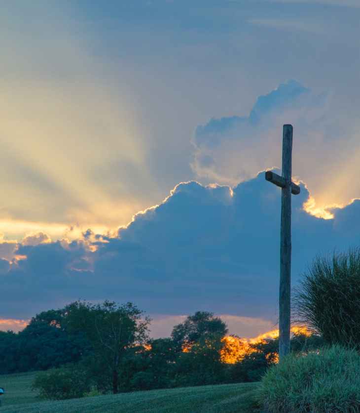 big wooden cross on green grass field under the white clouds